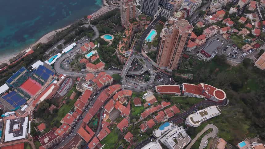 An aerial top-down drone shot slowly zooms in on the iconic hairpin turn and cityscape of Monte Carlo, Monaco, nestled against the blue sea