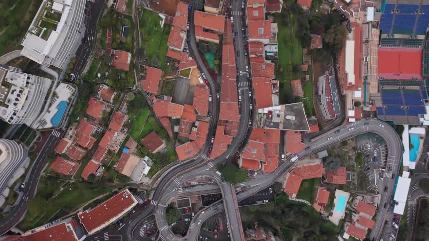 A slowly rising top-down aerial view captures the intricate network of winding roads and beautiful architecture in a lush, green hillside city