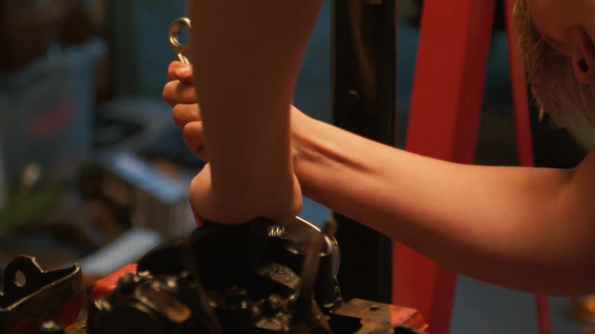 A close-up shot shows a mechanic's hands using a large wrench to tighten a bolt on a car engine in a garage
