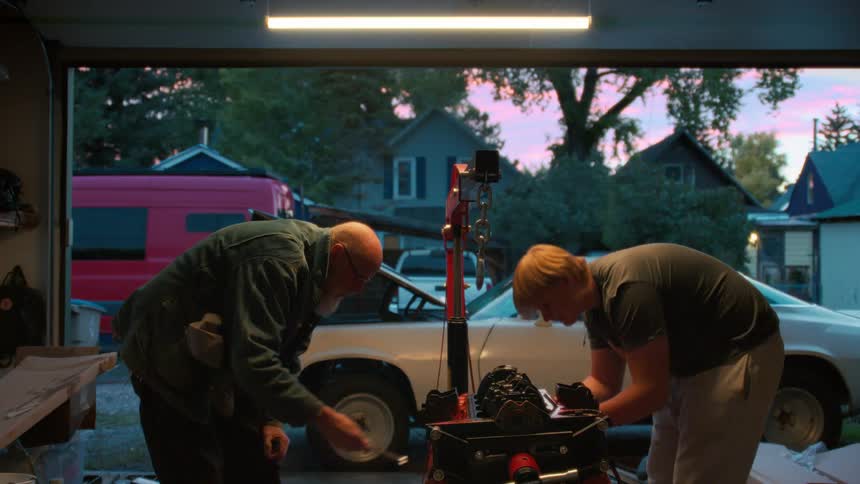 A father and son team up to rebuild a car engine in their garage as the sun sets