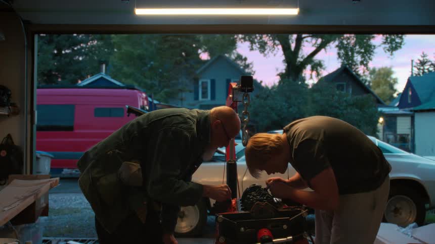 A father and son share a bonding moment as they work together on a car engine in their home garage at dusk