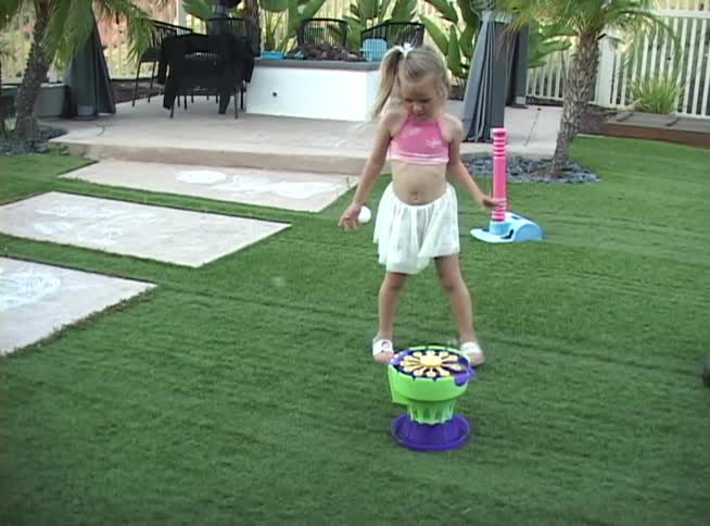 A young girl with a ponytail happily plays with a bubble-making machine in her grassy backyard