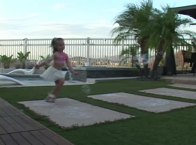 A happy young girl runs and plays with bubbles from a bubble machine in a modern backyard at dusk