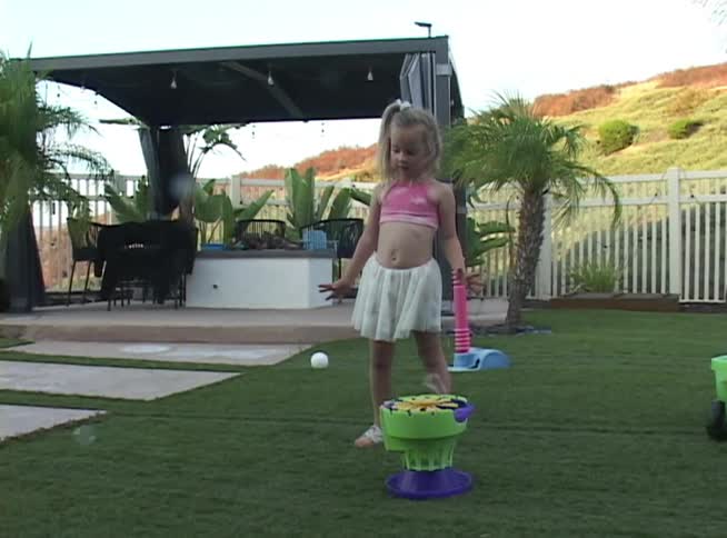 Slow motion of a little girl chasing bubbles from a bubble machine across the green lawn of a beautiful modern backyard