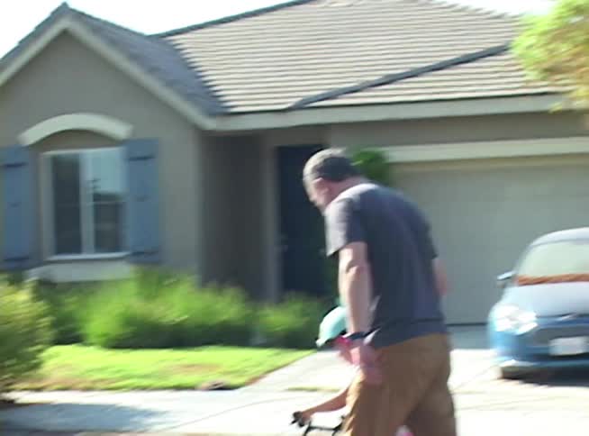A father teaches his young daughter how to ride a bicycle down a quiet suburban street on a sunny day