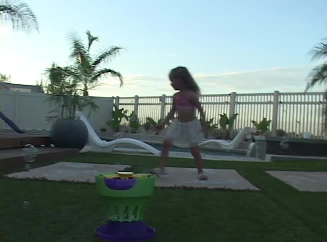Little girl plays with floating bubbles in a backyard near the pool at sunset