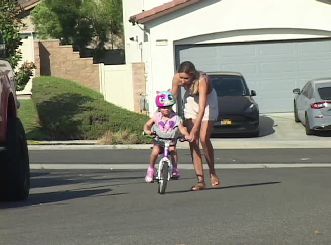 A mother patiently teaches her young daughter how to ride her first bicycle in their suburban neighborhood on a sunny day