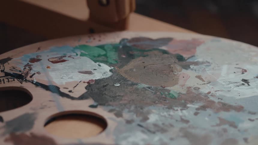 Close-up of a well-used wooden artist's palette with mixed paints on a studio easel