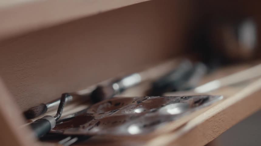 A detailed close-up shot of various artist's tools, including brushes and a paint palette, inside a wooden box