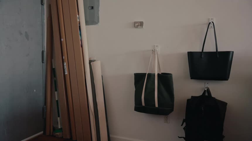Tote bags and a backpack hang on a white wall in a quiet, domestic entryway