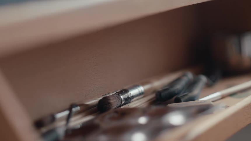 A detailed close-up shot of various paintbrushes and art supplies stored in a wooden container
