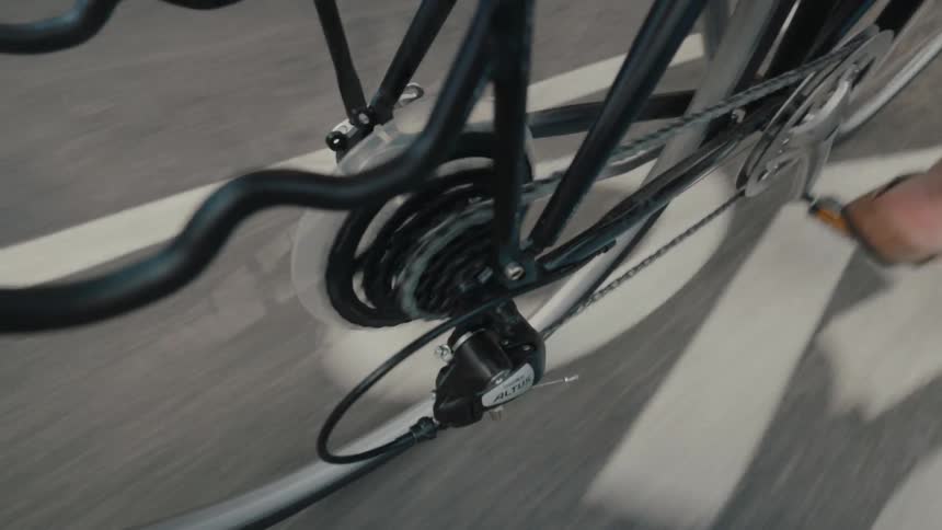 A slow-motion close-up of a bicycle's rear wheel, chain, and gears as a person pedals down a paved street