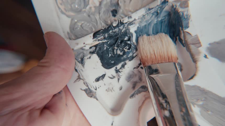Slow motion macro shot of an artist's brush gathering dark paint from a palette