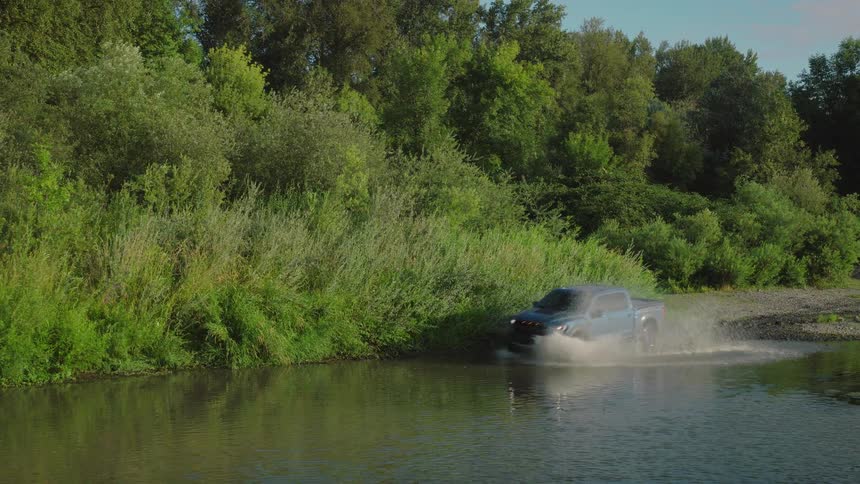 A blue pickup truck splashes through a river in a dense green forest on a sunny day
