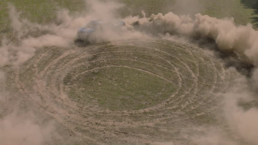 High angle slow motion shot of a blue pickup truck drifting in circles in a field, throwing up a huge cloud of dust