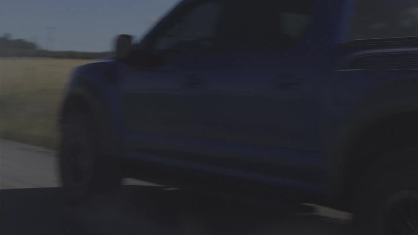 Side tracking shot of a blue Ford Raptor pickup truck kicking up dust and smoke as it drifts along a country road in slow motion