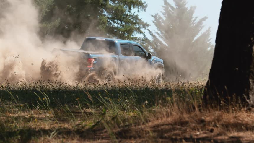 A powerful blue pickup truck does a burnout in a dry field, kicking up a massive cloud of dust in super slow motion