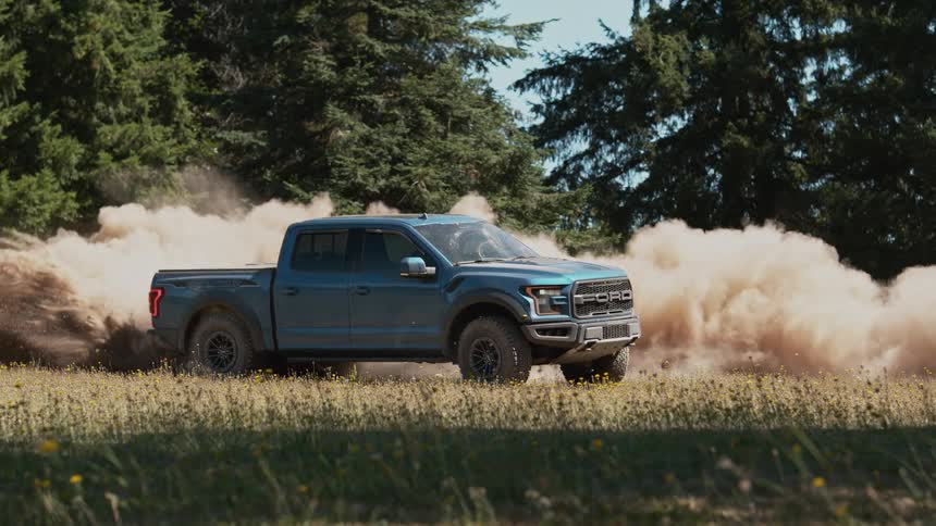 Cinemagraph of a powerful blue pickup truck kicking up a massive cloud of dust while off-roading in a field in super slow motion