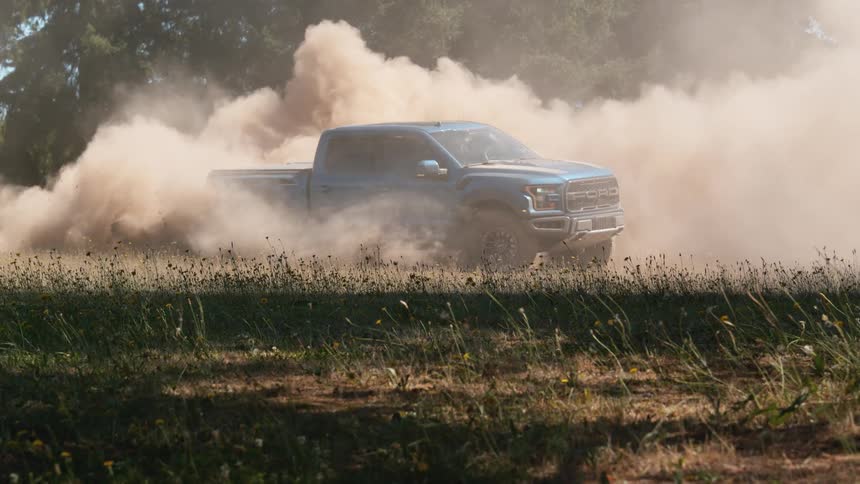 A powerful blue pickup truck kicks up a massive cloud of dust while doing a burnout in a dry field in cinematic slow motion