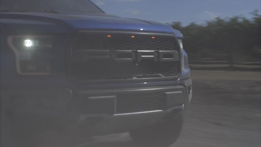 A powerful blue pickup truck drives in slow motion down a dusty country road, kicking up a huge cloud of dirt