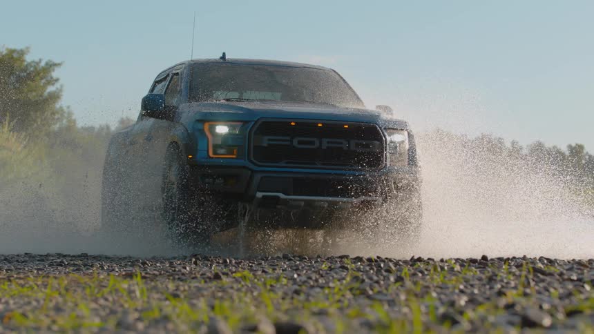 A blue off-road truck drives through a river, creating a dramatic splash in super slow motion