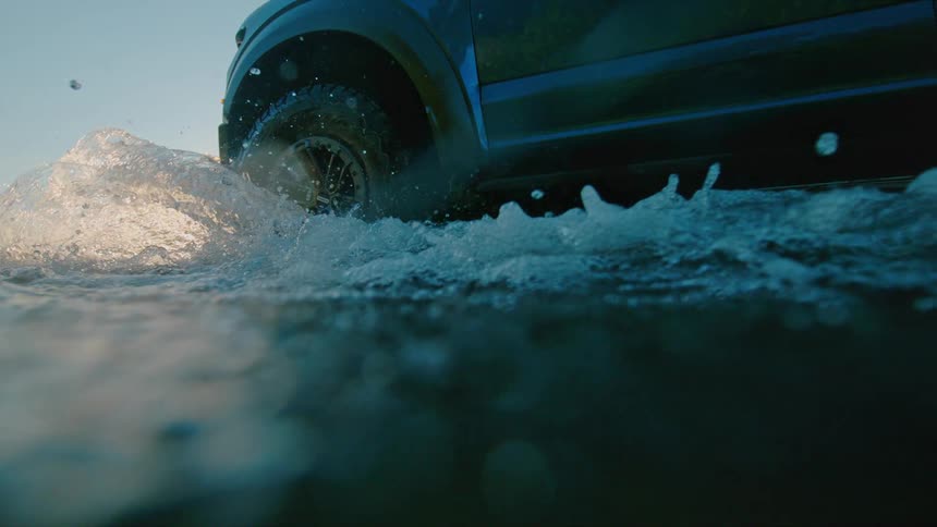 An off-road truck splashes through the water in dramatic slow motion with the camera becoming submerged at golden hour