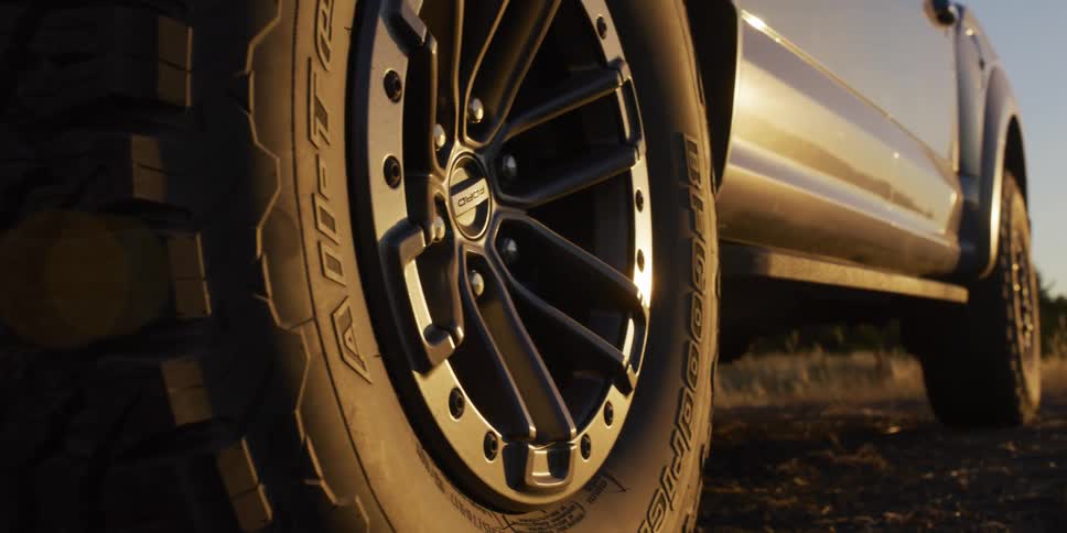 A slow cinematic dolly reveals a close-up of a rugged off-road truck tire and rim during a golden hour sunset