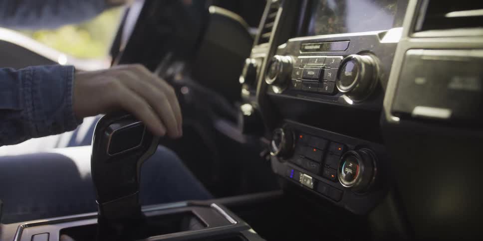 A driver shifts gears and turns the steering wheel inside a modern pickup truck