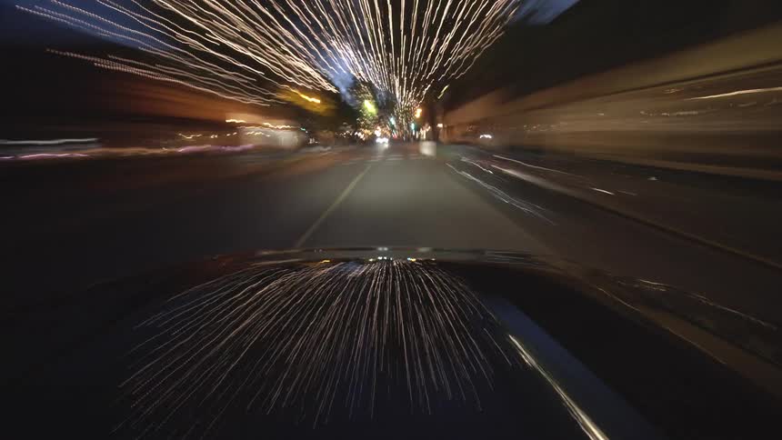Dynamic hyper-lapse from a car's hood captures a speedy drive through a city at night, transforming streetlights into vibrant, surreal light trails