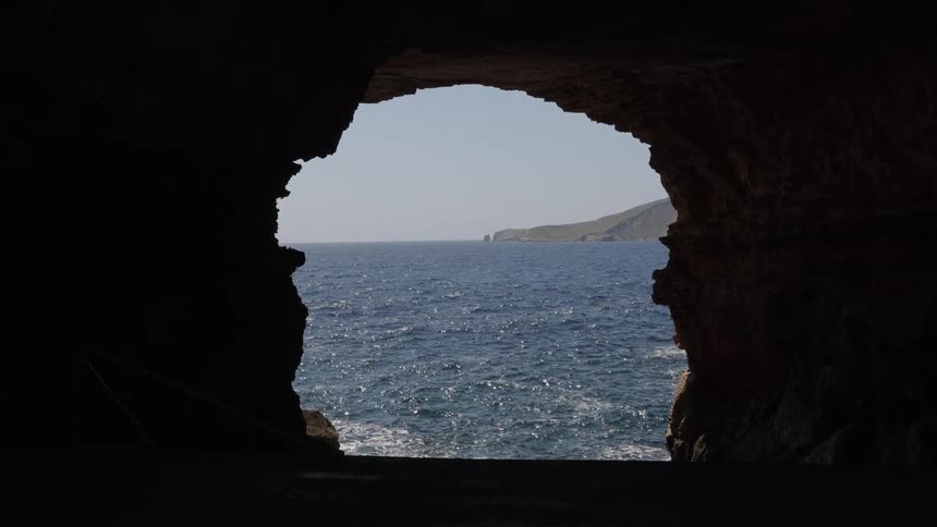 A serene view of the sparkling blue ocean and a distant coastline framed by the silhouette of a dark sea cave