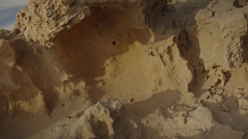 A slow, sliding close-up shot reveals the intricate, porous texture of eroded sandstone