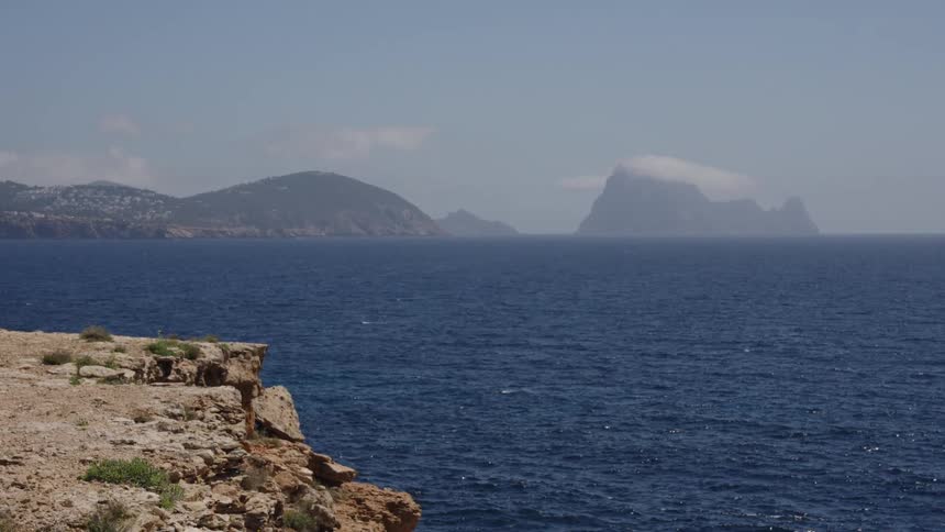 A scenic view from a rocky cliff overlooking the deep blue sea with distant islands on the horizon
