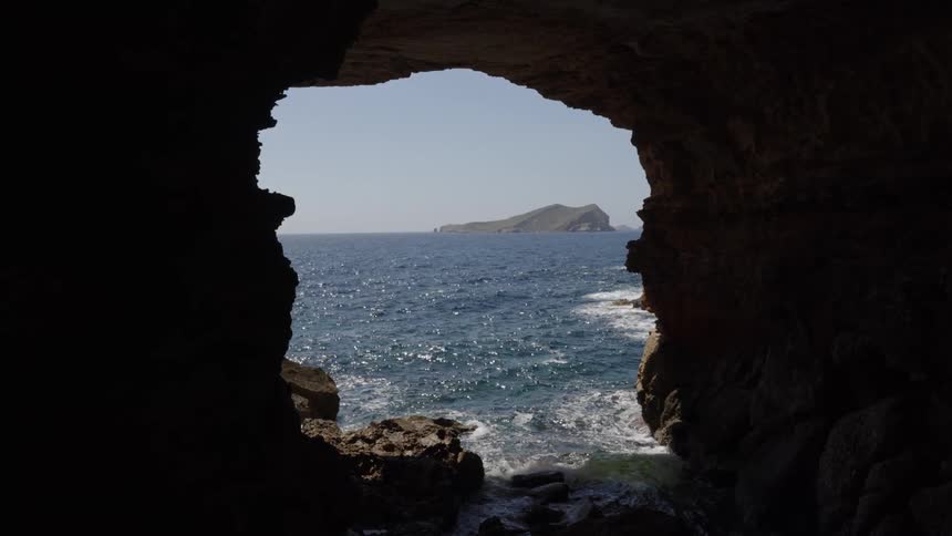 A serene view from inside a coastal cave looking out at the sunlit blue ocean and a distant island