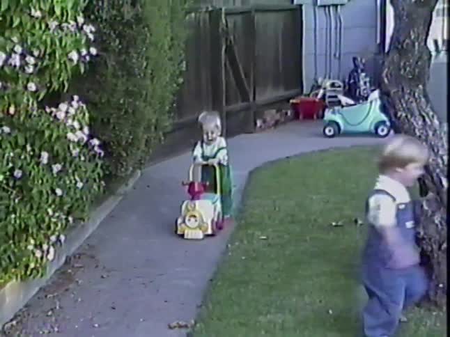 Vintage home movie footage of two happy toddlers playing with toys in a suburban backyard