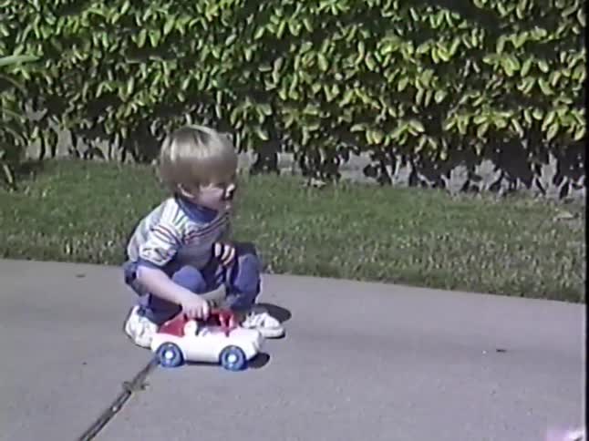 Happy toddlers play together on a sidewalk, ending with one boy running in slow motion in this vintage home movie