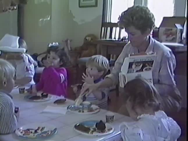 Vintage home movie footage captures a group of cute toddlers sitting at a table eating cake and ice cream at a birthday party