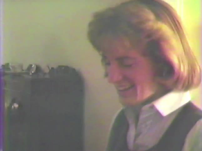 A woman with a vintage 1980s hairstyle smiles and laughs while socializing at an indoor party