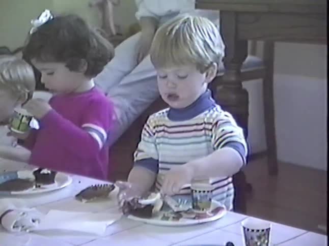 A group of cute toddlers eat cupcakes together at a birthday party in a nostalgic home video
