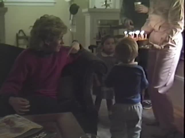 A happy woman is surprised with a birthday cake while surrounded by her family and friends in a cozy living room