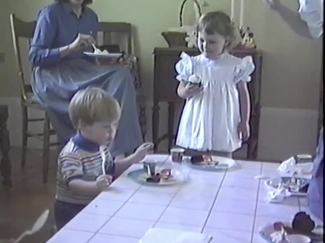 Vintage home movie captures a mother lighting birthday candles on a brownie for her young son as other children watch