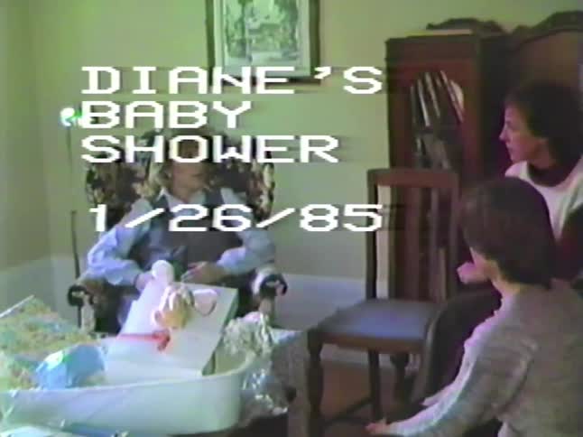 A pregnant woman sits in a chair surrounded by gifts and friends at her baby shower in this vintage 1985 home movie
