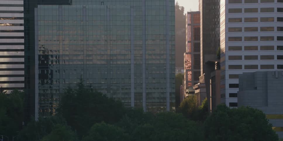 A slow-motion tracking shot reveals the downtown Portland, Oregon skyline, including the Hawthorne Bridge, as a warm sun flare washes over the city