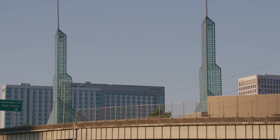 A smooth tracking shot reveals the iconic twin glass spires of the Oregon Convention Center behind busy highway overpasses in Portland