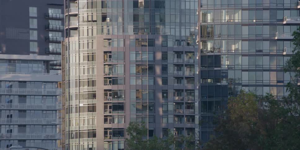 A slow zoom out timelapse of morning light and shadows moving across modern glass apartment buildings in a city