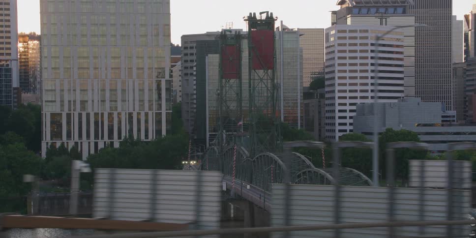 An aerial tracking shot reveals the Hawthorne Bridge over the Willamette River against the Portland skyline during a hazy golden hour sunset
