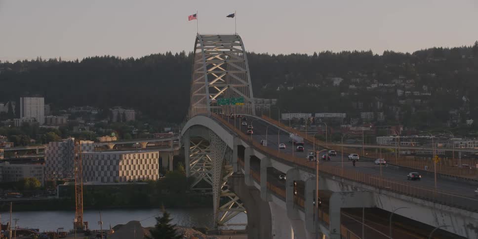 An aerial tracking shot of traffic flowing over the iconic Fremont Bridge in Portland, Oregon at sunset, with the city and hills in the background