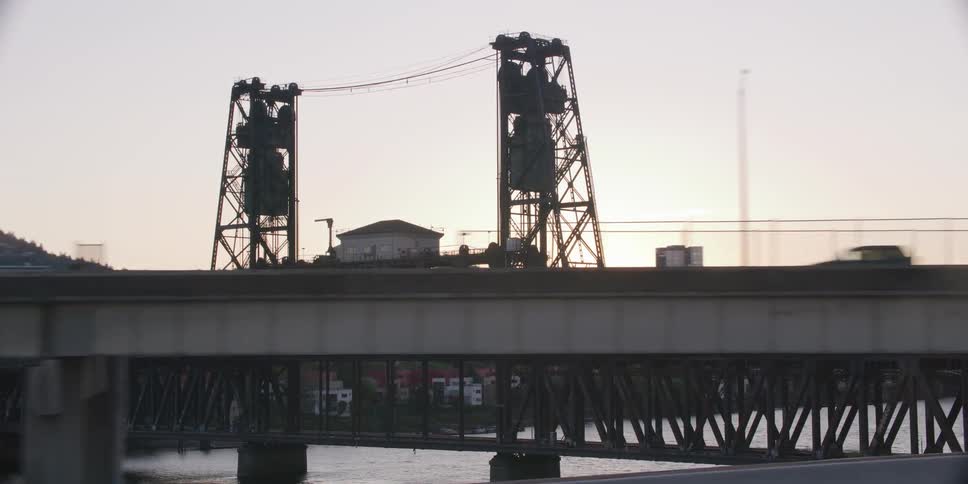A smooth tracking shot reveals the iconic Steel Bridge in Portland, Oregon silhouetted against the city skyline at dusk