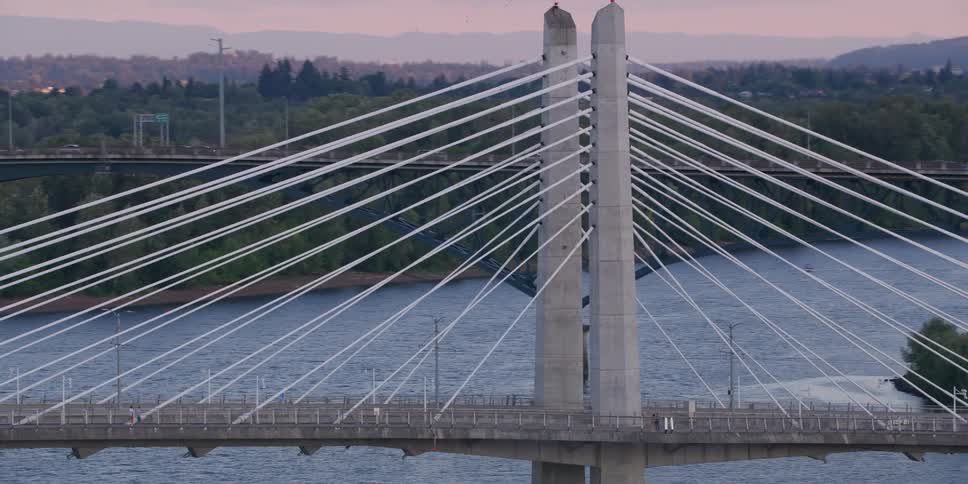 A majestic aerial shot pans across the Tilikum Crossing bridge over the Willamette River in Portland, Oregon, during a beautiful sunset