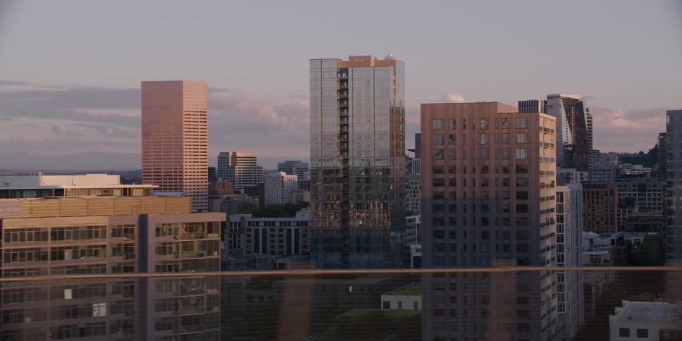 A tracking shot reveals the downtown Portland, Oregon skyline with skyscrapers glowing in the soft light of a beautiful sunset