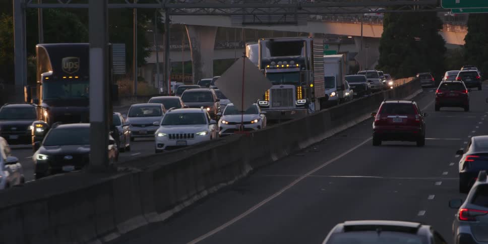 A slow-motion telephoto shot shows heavy rush hour traffic moving slowly along a city freeway at dusk